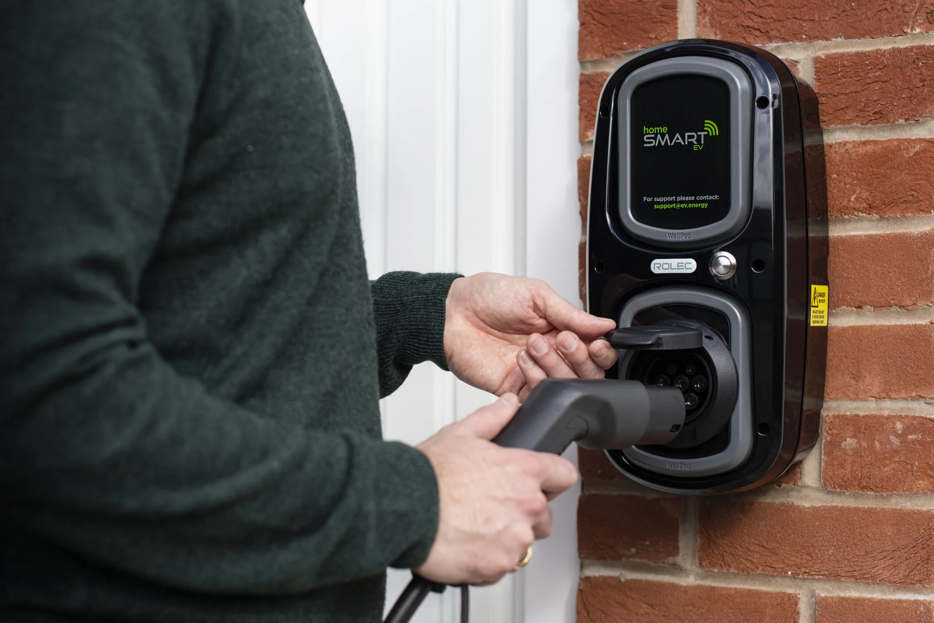 Connecting a charging cable to a wall-mounted home EV charger.